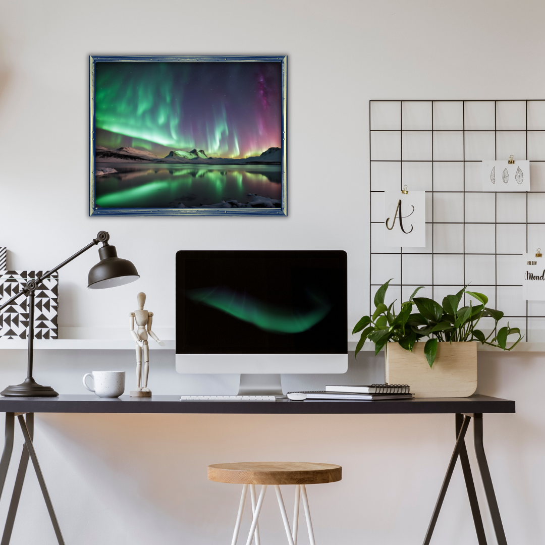 Framed Aurora Borealis print above a minimalist desk with a lamp, a plant, and a computer.