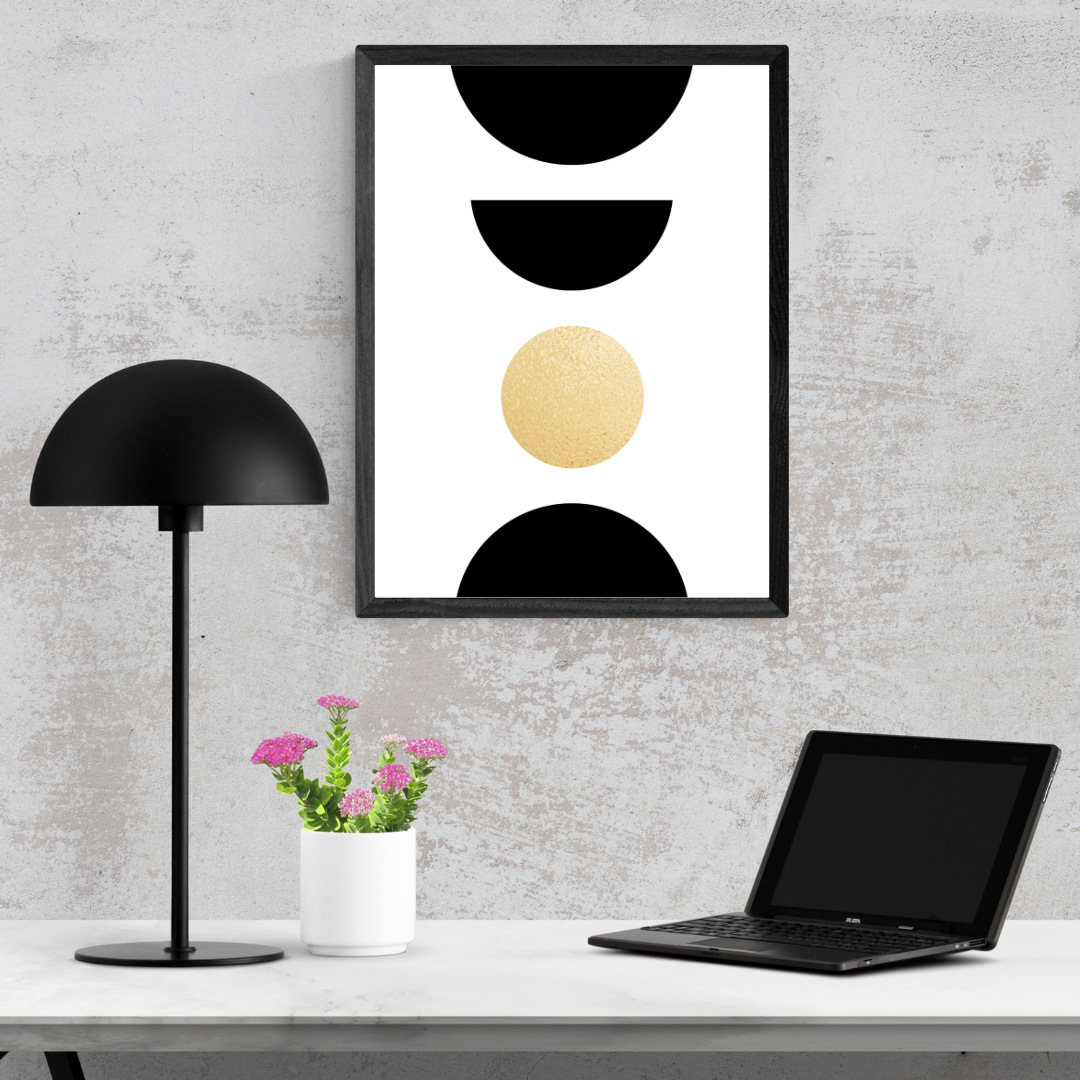 Modern home office setup with boho black and gold stacked shapes art, lamp, laptop, and plant on a white desk.