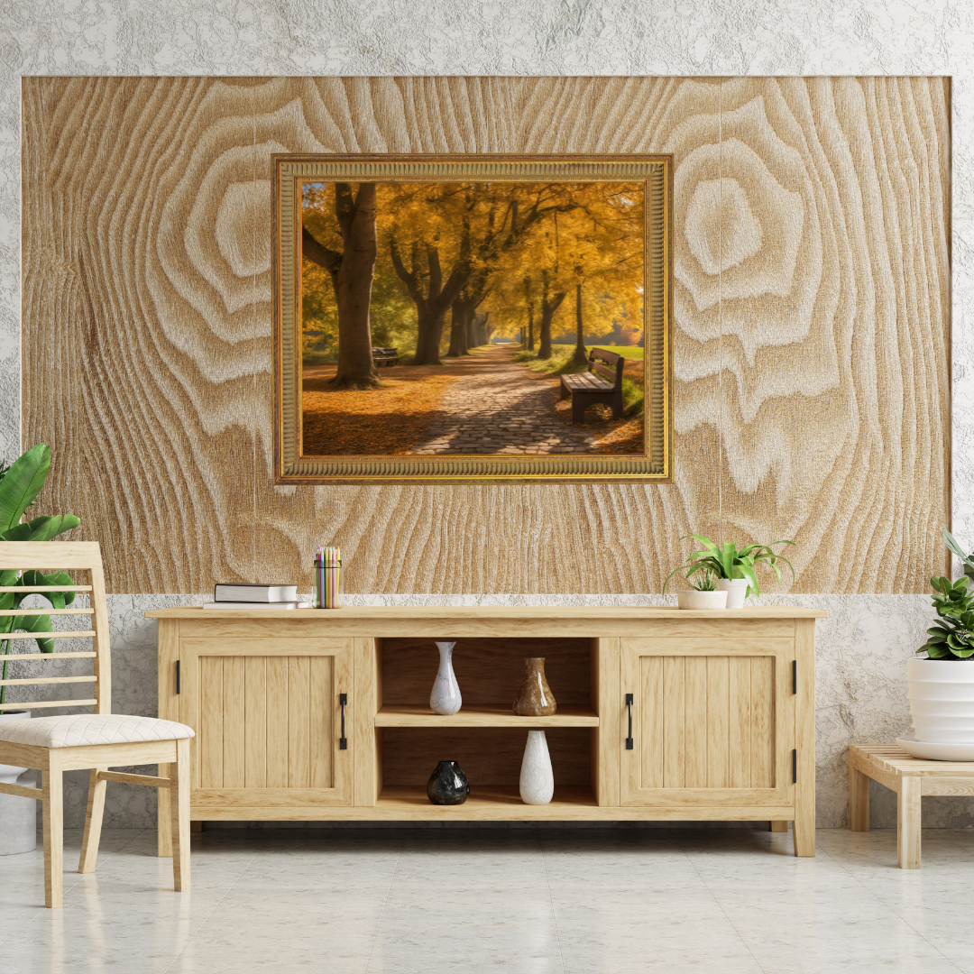 Framed autumn path print, above a light‑wood sideboard with vases, books and a chair.