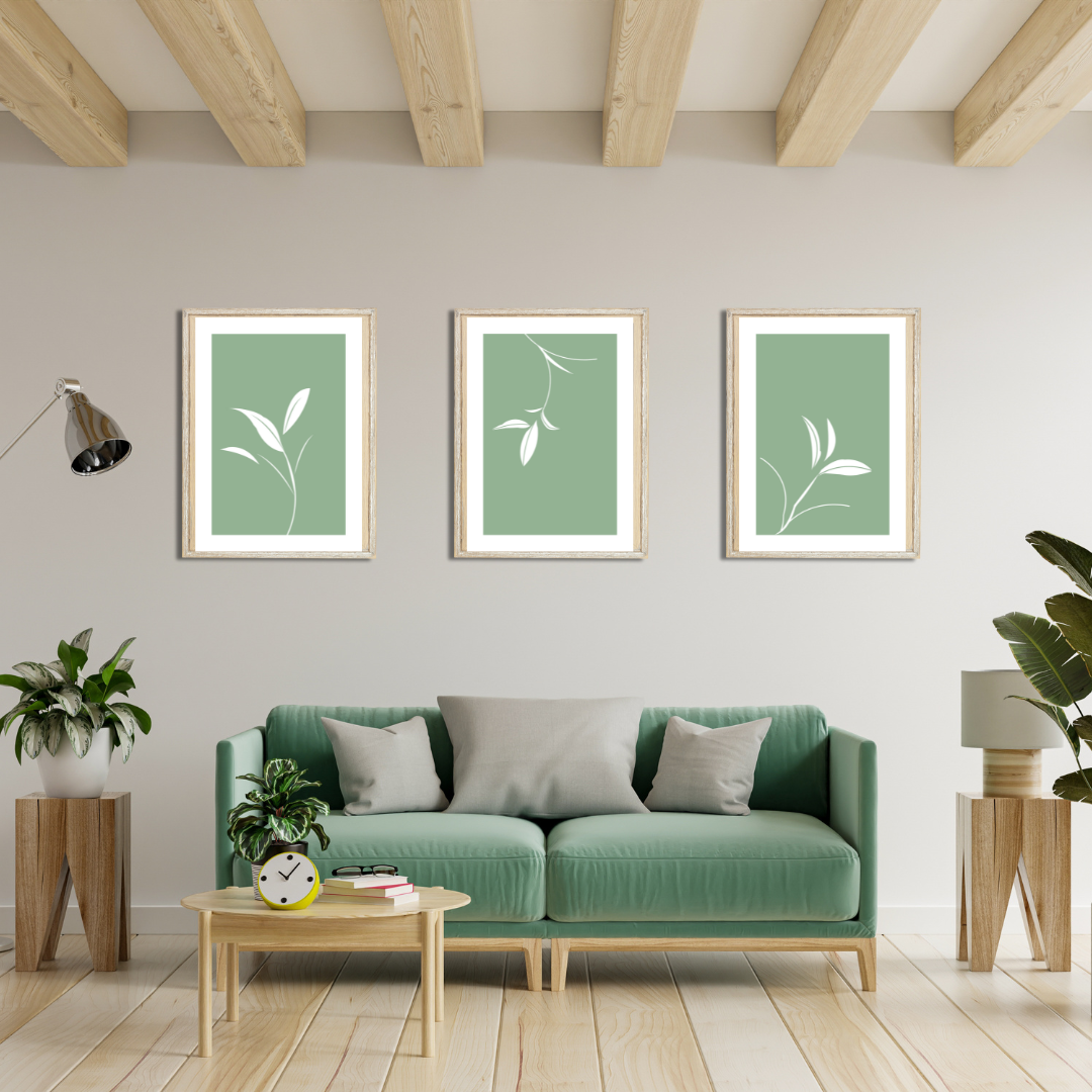 Set of three minimalist white botanical prints on sage green, framed above a green velvet couch with wooden decor.