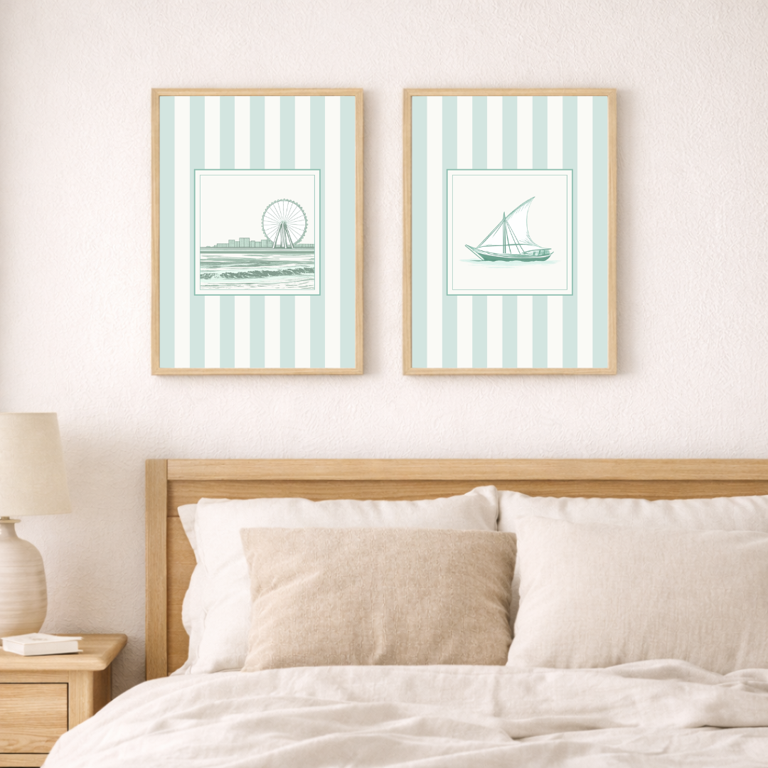 Two framed beach-themed coastal prints of a dhow and the Dubai Eye with striped patterns above a bed in a neutral coastal setting.