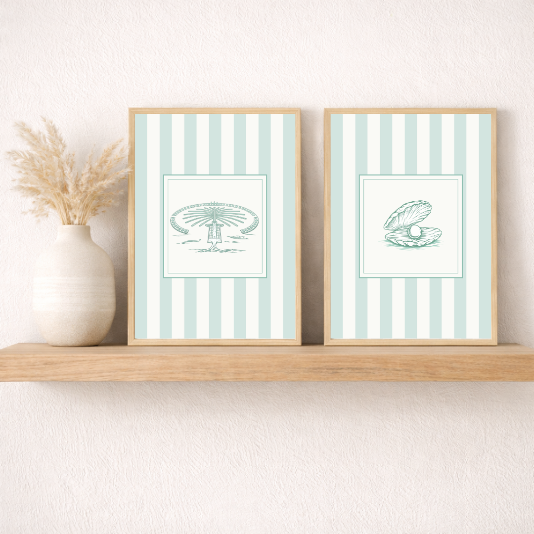 Two framed coastal prints of the Dubai Palm and an oyster with striped backgrounds in sea green on a wooden shelf.