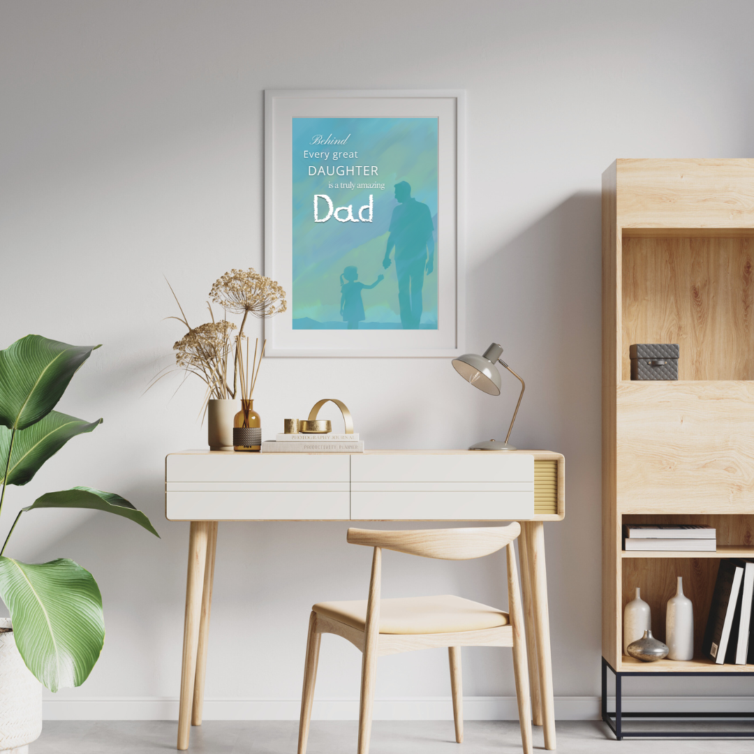 Warm home study with light wood desk and bookshelf featuring framed “Amazing Dad” quote print on a neutral wall.