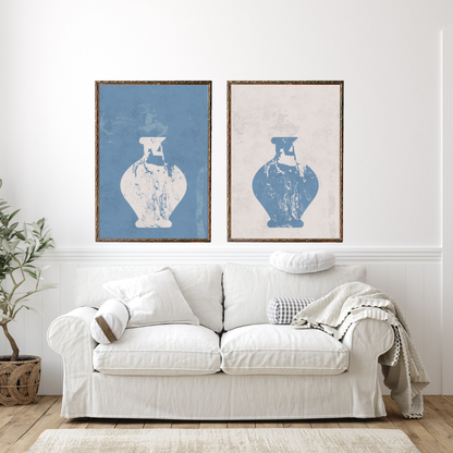 White sofa with decorative pillows in a room with two framed Wabi Sabi wall art pieces of blue and beige vases.