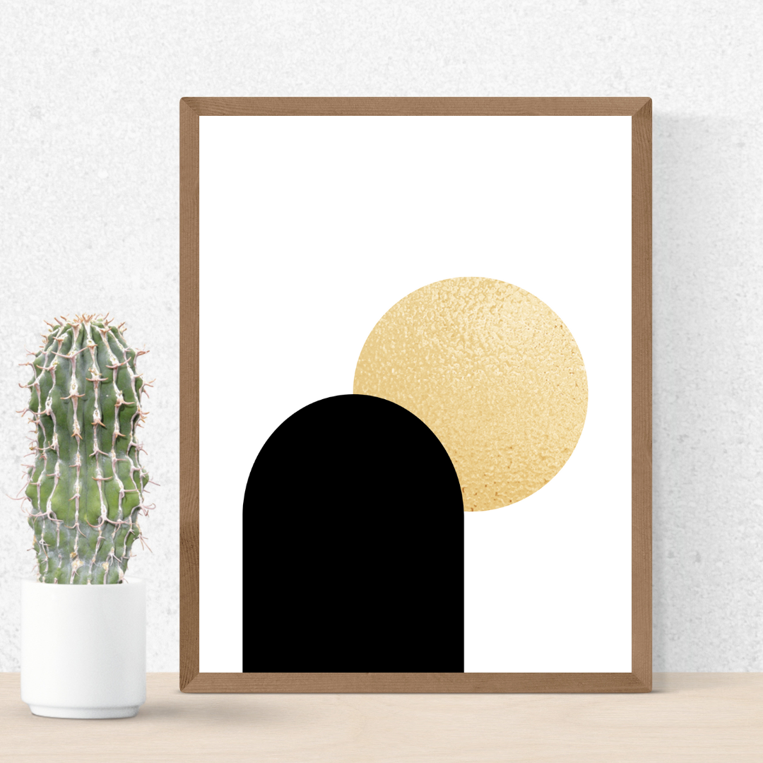 Framed boho style abstract art print with black and gold shapes next to a cactus plant on a neutral wall.