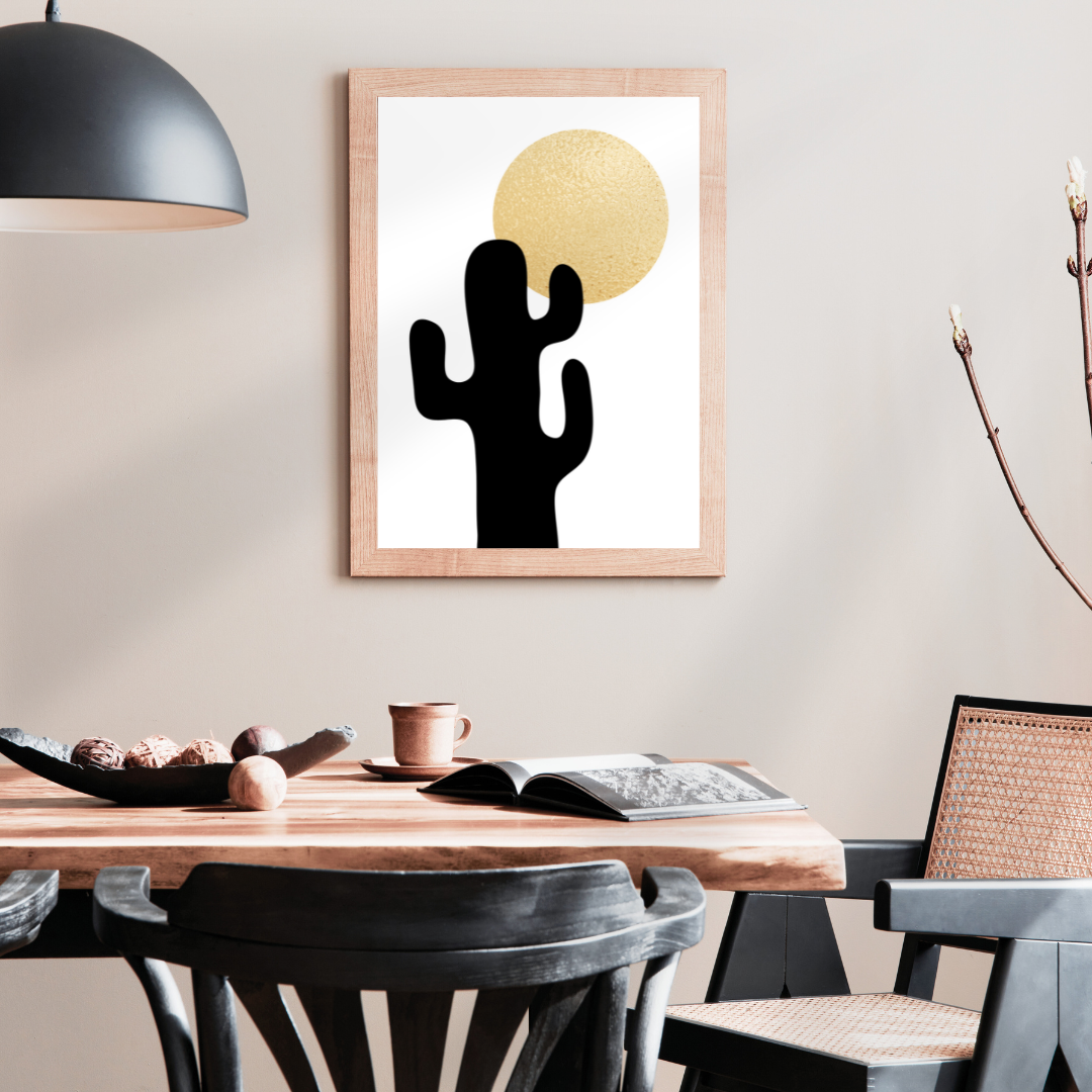 Dining room with a wooden table, chairs, and a framed artwork of a black cactus and gold sun on the wall.