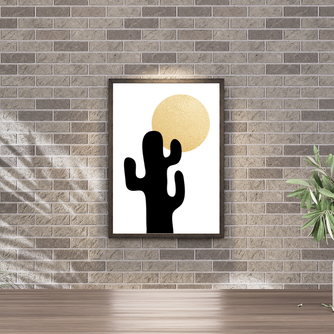 Framed boho style artwork of a black cactus and gold sun on an earthy brick wall with plant decor.
