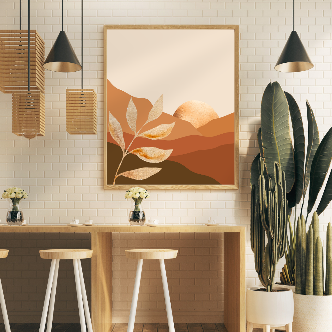 Framed printable boho wall art of radiant gold sun hiding behind an earth-toned layered mountain above a coffee shelf.