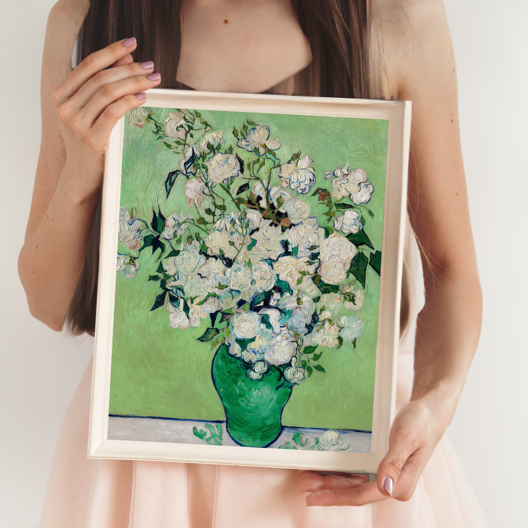 Person holding a framed painting of white flowers in a green vase on a light background