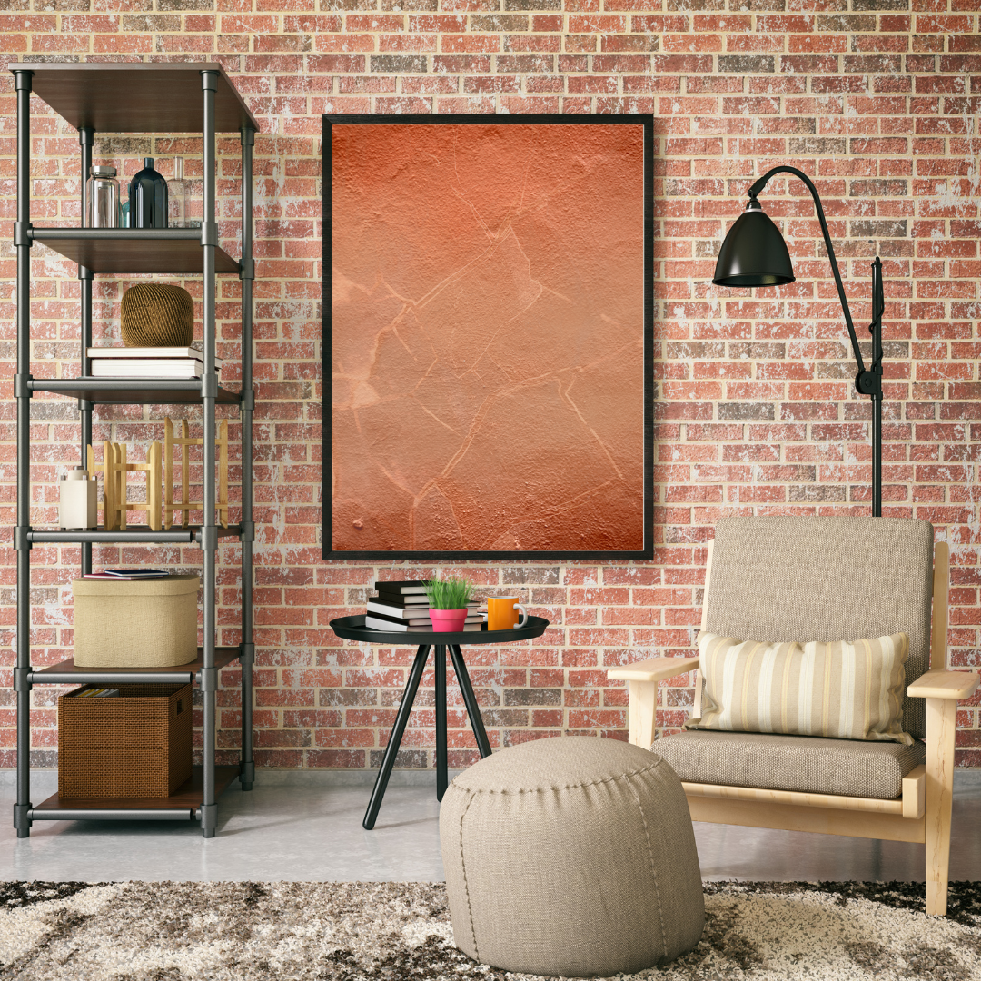 Framed Wabi Sabi wall are of broken glass against a textured terracotta background mounted on a brick wall, in a reading nook with a bookshelf, chair, ottoman, and decorative items.